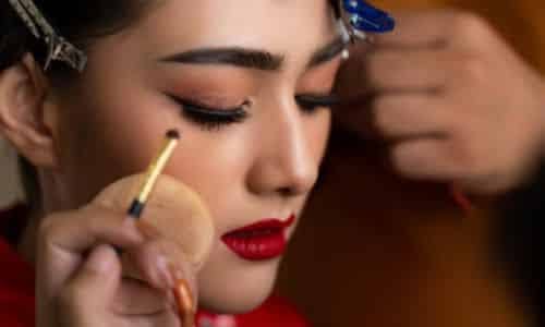 Donna viene truccata da un make up artist con un ombretto rosso