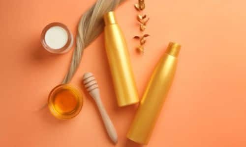 foto con sfondo arancio di una ciocca di capelli bionda, miele e prodotti con confezioni arancioni a base di miele e olio