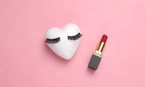 sfondo rosa con un cuore bianco con sopra le ciglie finte, tipiche del trucco anni venti e il rossetto rosso